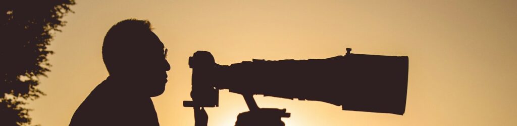 silhouette of man holding camera during sunset