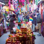 Colorful market aisle in England bustling with shoppers and vibrant textiles.