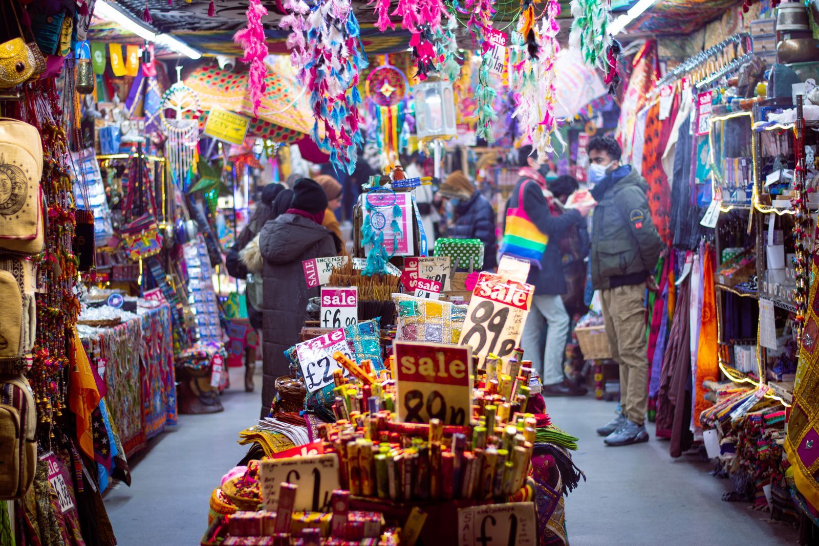 Colorful market aisle in England bustling with shoppers and vibrant textiles.