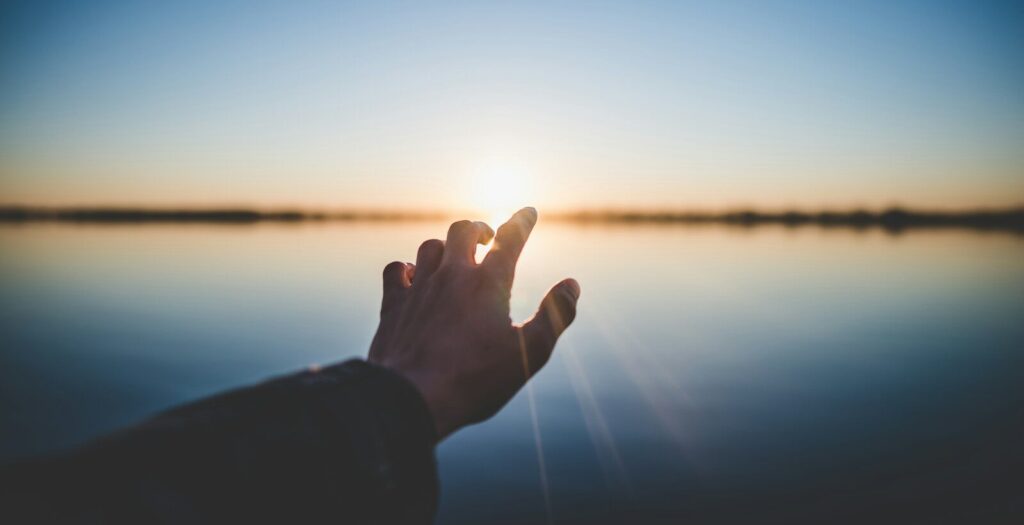 landscape photography of person's hand in front of sun
