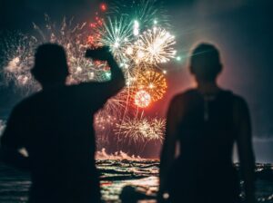 Silhouetted figures watching fireworks display over water.
