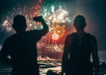 Silhouetted figures watching fireworks display over water.
