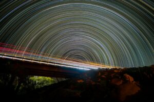 Star trails arc across the night sky above light trails.